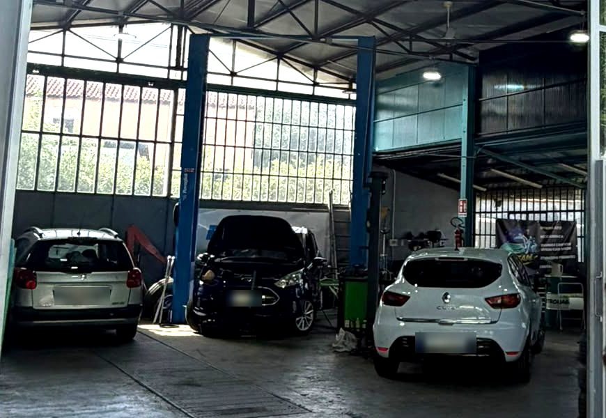 Interno dell'officina E.R.TEAM: tre auto in lavorazione, i ponti sollevatori blu e le vetrate del capannone